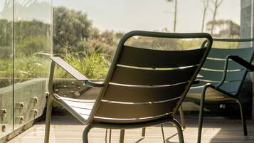 Una terraza de madera con una silla de metal y barandilla de vidrio.