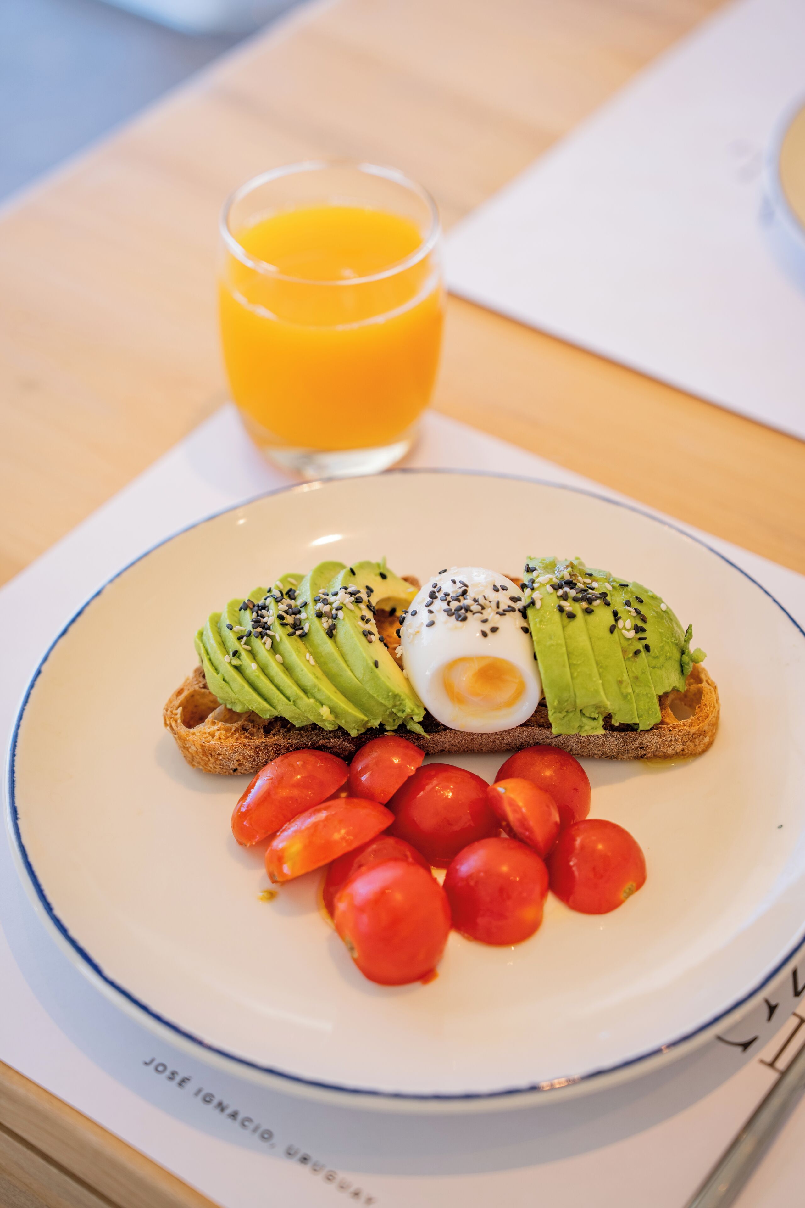 Une assiette avec des toasts à l’avocat, un œuf poché et des tomates cerises, accompagnée d’un verre de jus d’orange.