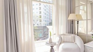 A room with a white sofa, a lamp, and a view of buildings through large windows. - Keypad Hotel - Nhân Hòa (Hanoi)