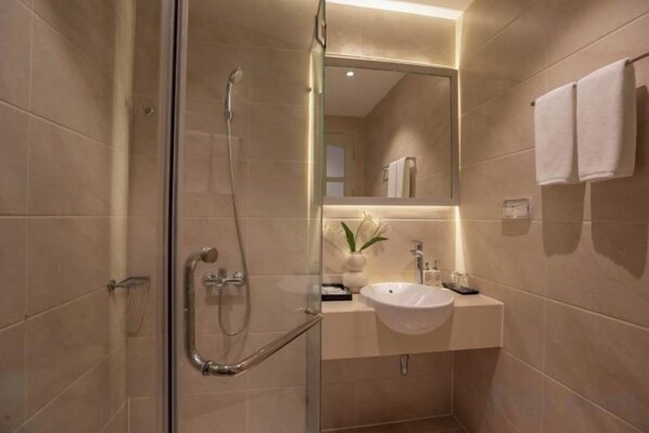 A modern bathroom with a glass-enclosed shower, a sink with a mirror above, and a towel rack on the wall. - Keypad Hotel - Nhân Hòa (Hanoi)