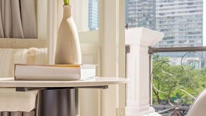 A balcony with a view of a cityscape, a white vase with a plant, and a stack of books on a white table. - Keypad Hotel - Nhân Hòa (Hanoi)