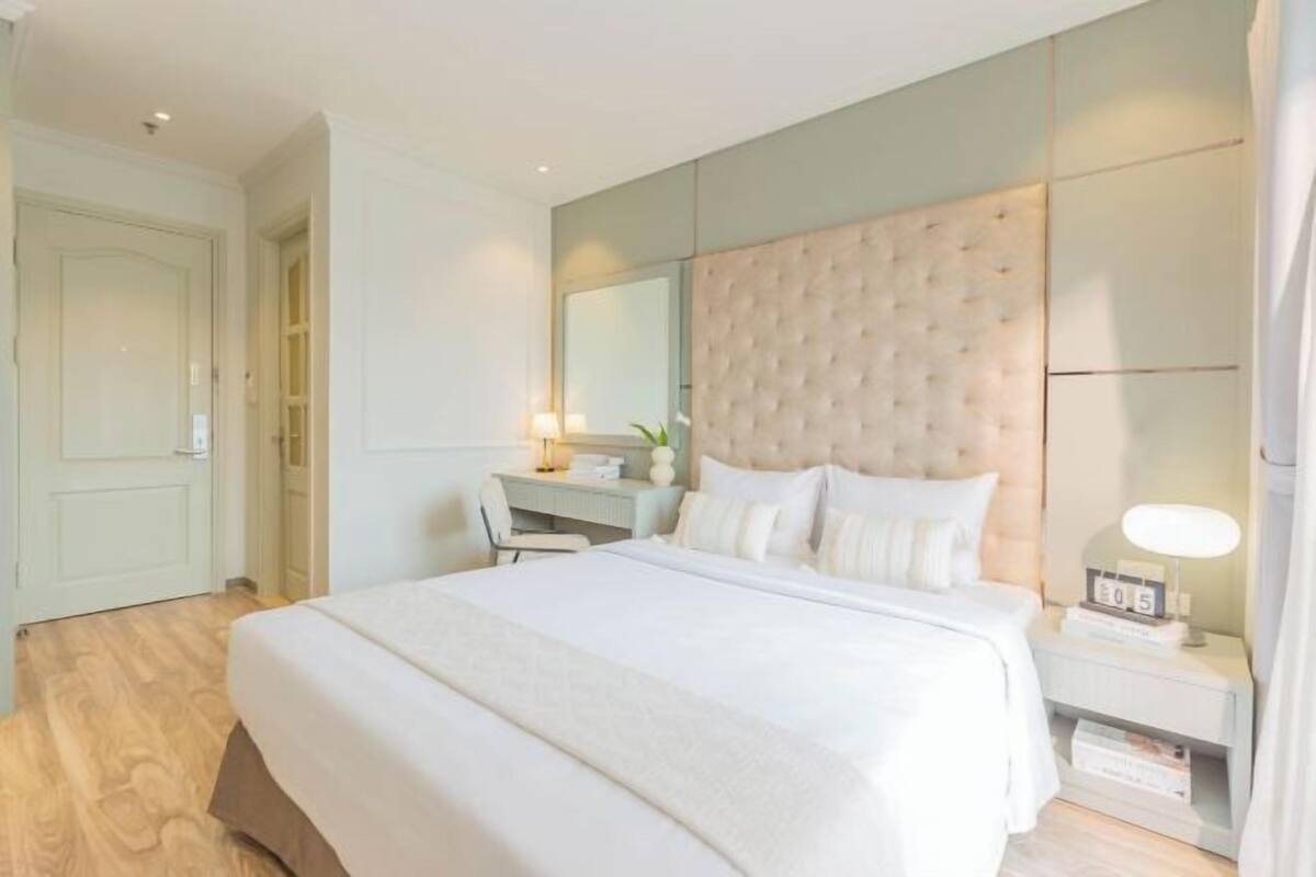 Habitación de hotel con una cama grande, un escritorio, una silla, una mesita de noche con lámpara y un armario.