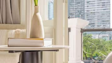 A table with a vase and a book, a window with a view of buildings, and a balcony railing.