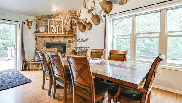 A dining area with a stone fireplace, mounted deer heads, and a large window. - Pet Friendly Cabin w/ Hot Tub: 5 mi to River (Wisconsin Dells)