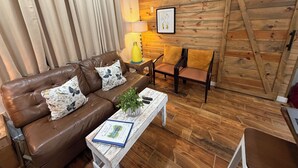 A cozy living room with a brown leather sofa, a wooden wall, and a wooden floor. - Quiet retreat near Anthony’s chapel & Garvan Gardens (Hot Springs)