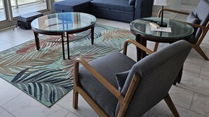 A modern living room with a sectional sofa, two glass-top coffee tables, and a patterned rug.