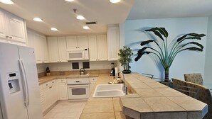 A modern kitchen with white cabinets, a built-in microwave, a refrigerator, a sink, and a dining area with a table and chairs.