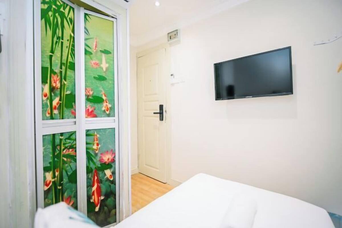 A hotel room with a bed, a television mounted on the wall, and a sliding glass door with a floral design.
