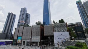 A modern urban plaza with high-rise buildings, a prominent Prada store, and a Balenciaga store.