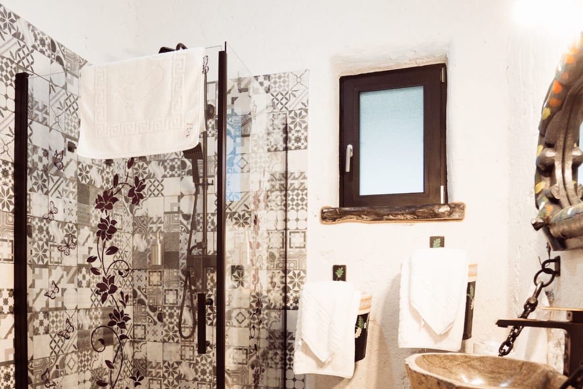 A bathroom with patterned tiles, a glass shower enclosure, a wooden basin, and a mirror with a wooden frame.