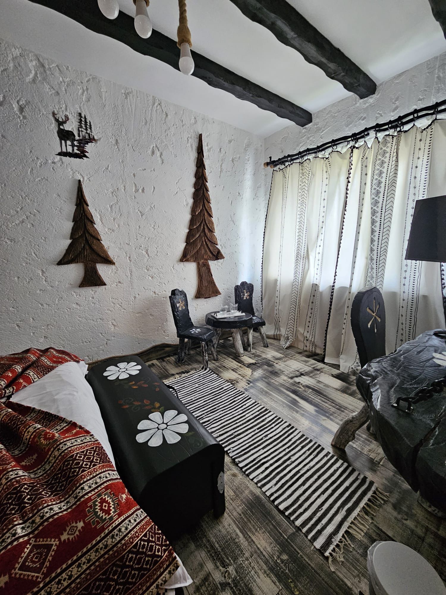 A cozy room with a bed, a small table, chairs, and a window with curtains.