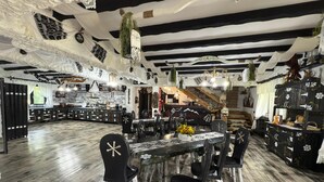 A rustic interior with a wooden dining table, black chairs, and a kitchen area with a bar. - Agi Traditional  (Bran)