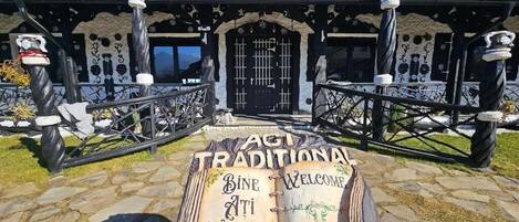 A traditional building with a stone facade, a black door, and a signboard with 'ACT TRADITIONAL' and 'BINE ATI VENIT!' written on it.