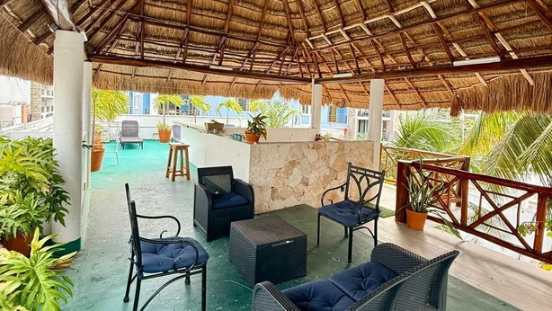 An outdoor lounge area with wicker furniture and a thatched roof. - Traveler SOLO (Playa del Carmen)