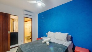A bedroom with a bed, a nightstand, a red bench, a ceiling fan, and a bathroom visible through an open door. - Fully Equipped Apartments Just Steps From Barra Beach and Barra Lighthouse - Csfs (Salvador)