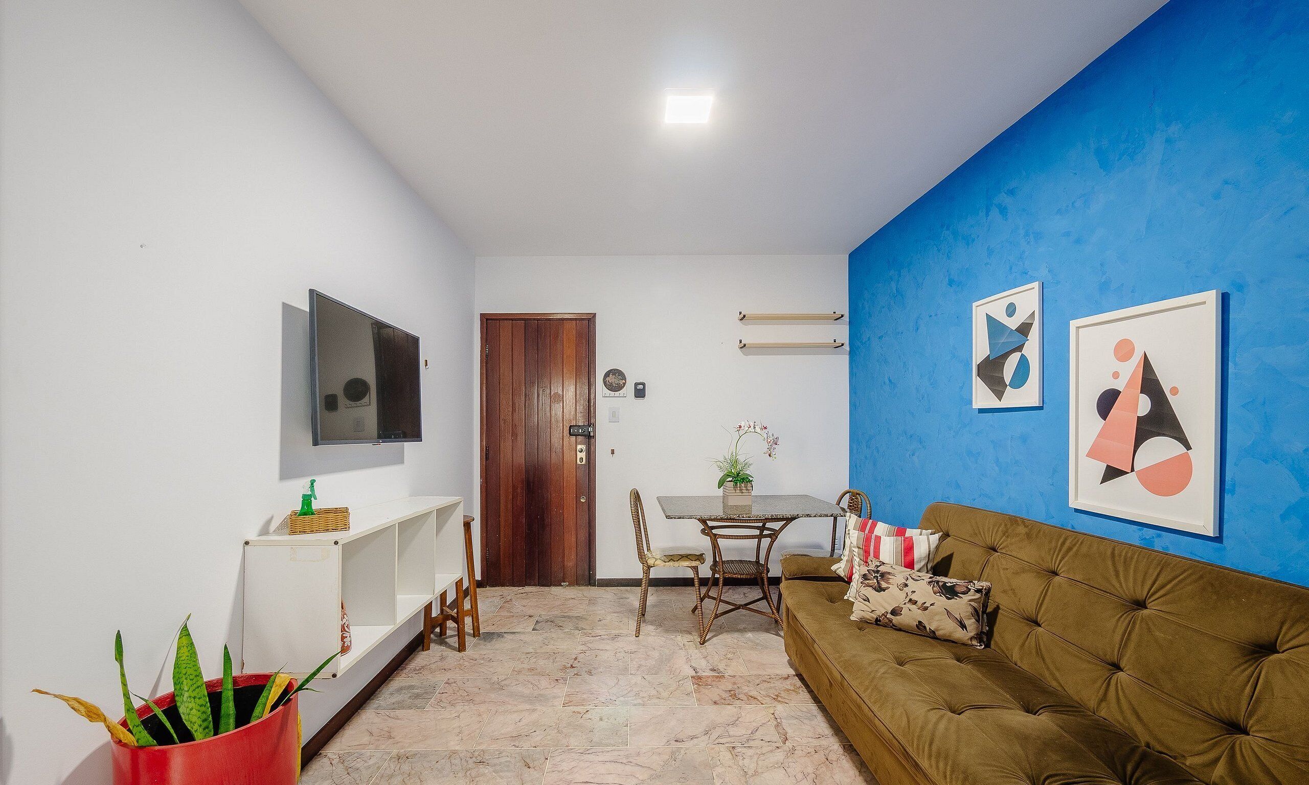 Un soggiorno con un divano marrone, una televisione montata a parete, un tavolo da pranzo con sedie e una parete decorata in blu.