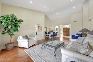 A spacious living room with a large plant, white furniture, and a dining area with blue chairs. - Wonderful 3-bedroom house in Peoria (Peoria)