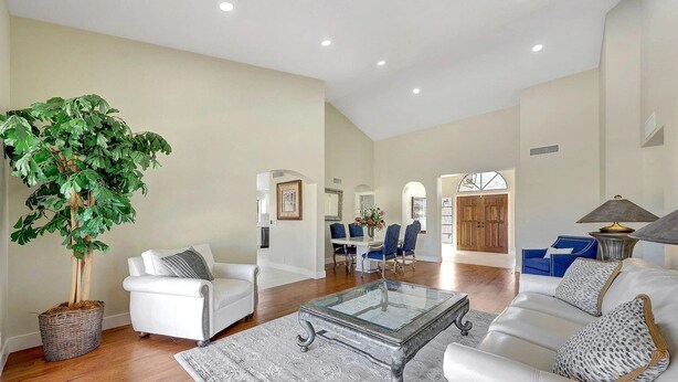 A spacious living room with a large plant, white furniture, and a dining area with blue chairs.
