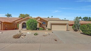 A single-story house with a garage, a landscaped front yard with rocks and shrubs, and a clear blue sky.