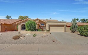 A single-story house with a garage, a landscaped front yard with rocks and shrubs, and a clear blue sky.