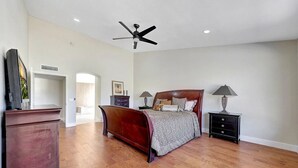 A spacious bedroom with a large bed, a ceiling fan, and a TV on a dresser.