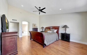 A spacious bedroom with a large bed, a ceiling fan, and a TV on a dresser.