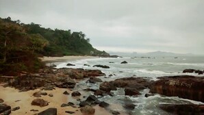 A rocky beach with waves crashing onto the shore, a sandy beach, and dense greenery on the left.