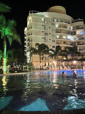 Ein Hotel bei Nacht mit Schwimmbad, Palmen und Terrassen.