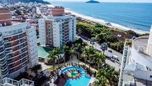 A high-rise hotel with multiple balconies, a central pool with a colorful design, and a view of the beach and ocean.