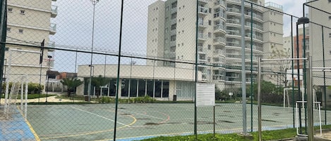 Cancha deportiva cercada con aro de baloncesto, rodeada por una valla de malla.