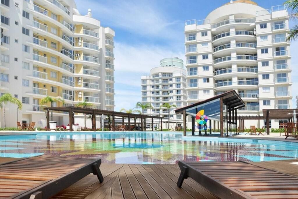 Uma piscina com espreguiçadeiras de madeira, cercada por edifícios com varandas.