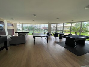 Um espaço interior moderno com mesa de bilhar, área de estar e grandes janelas que oferecem vista para o exterior.