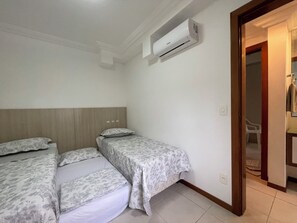Quarto com duas camas, uma cabeceira de madeira e um ar condicionado fixado na parede.