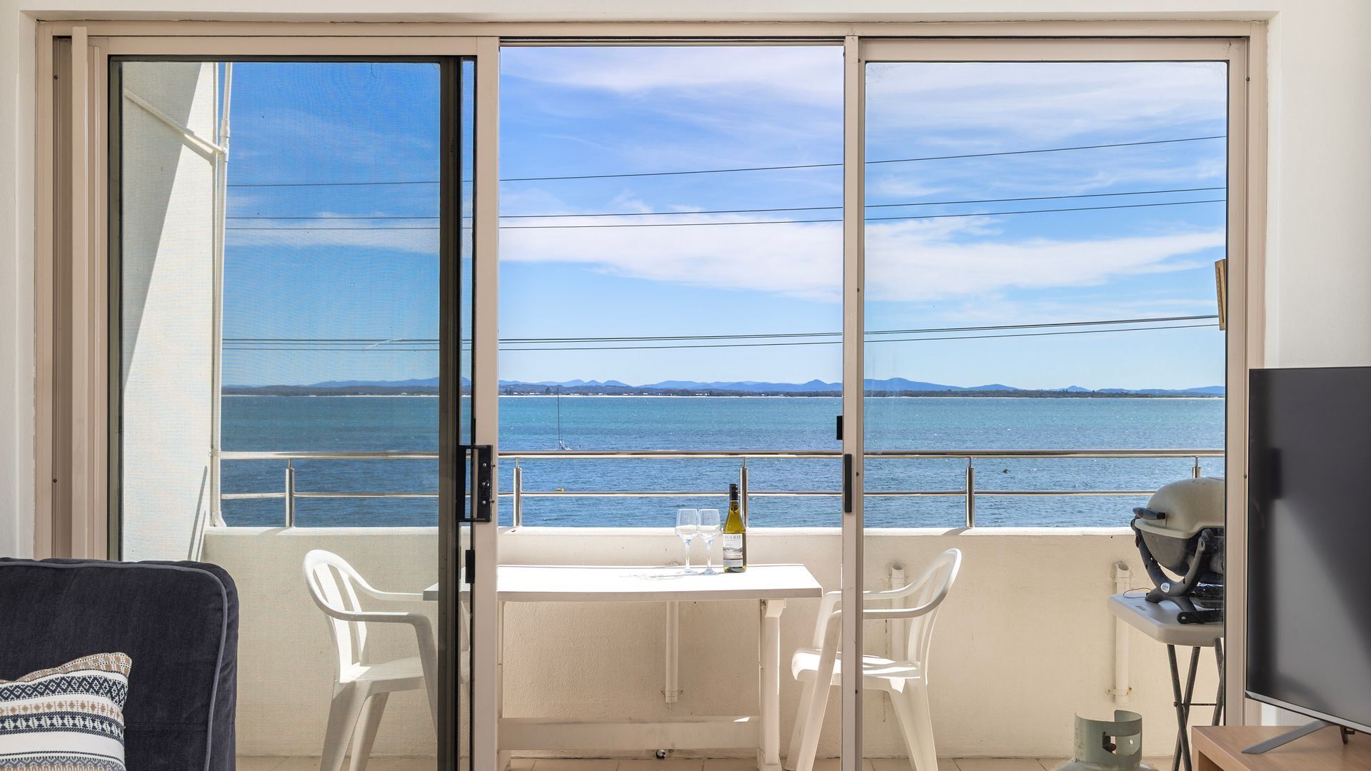 A balcony with a table, two chairs, a bottle of wine, and a TV.