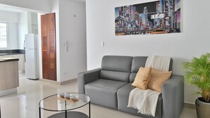 Un salon moderne avec un canapé gris, une table basse en verre et un tableau représentant un paysage urbain accroché au mur.