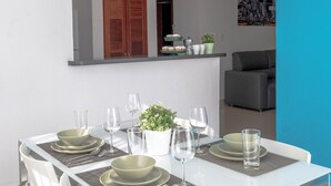 Un espace repas moderne avec une table blanche dressée pour quatre personnes, des chaises blanches et une cuisine en arrière-plan.
