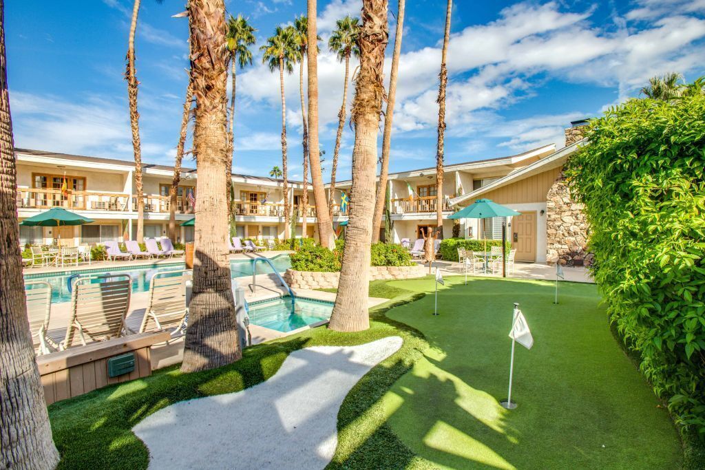 A pool area with lounge chairs and palm trees, a putting green, and a flagstick.