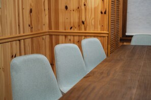 Un salón de conferencias con un panel de pared de madera, una mesa de madera y tres sillas de color gris claro.