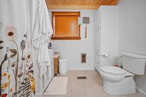 Un baño con inodoro, cortina de ducha con motivos florales, ventana con persianas y un perchero para toallas.