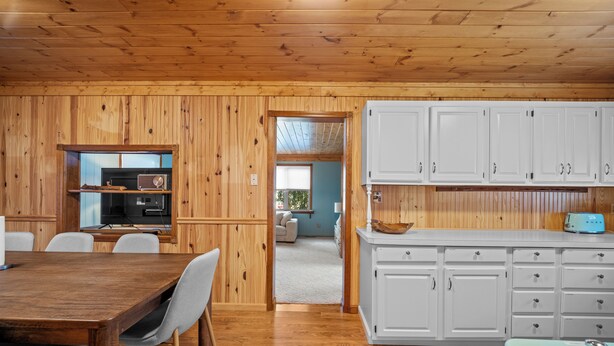 A wooden-paneled room with a dining table, chairs, a kitchen area with white cabinets, and a blue appliance. - Quaint 2-bedroom cottage in Houghton Lake - quick walk to lake (Houghton Lake)