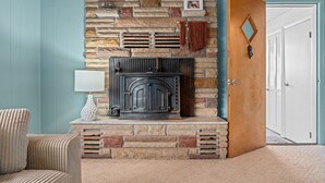 A stone fireplace with a modern design, a wooden door, and a view into a room with a light blue wall. - Quaint 2-bedroom cottage in Houghton Lake - quick walk to lake (Houghton Lake)