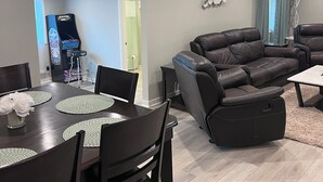 Un soggiorno moderno con un divano in pelle marrone scuro, un tavolo da pranzo con sottopiatti e una televisione a schermo piatto sullo sfondo.