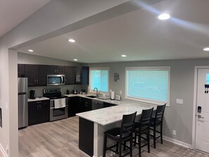 Una cocina moderna con armarios oscuros, electrodomésticos de acero inoxidable, encimera de granito y una zona de bar con sillas.