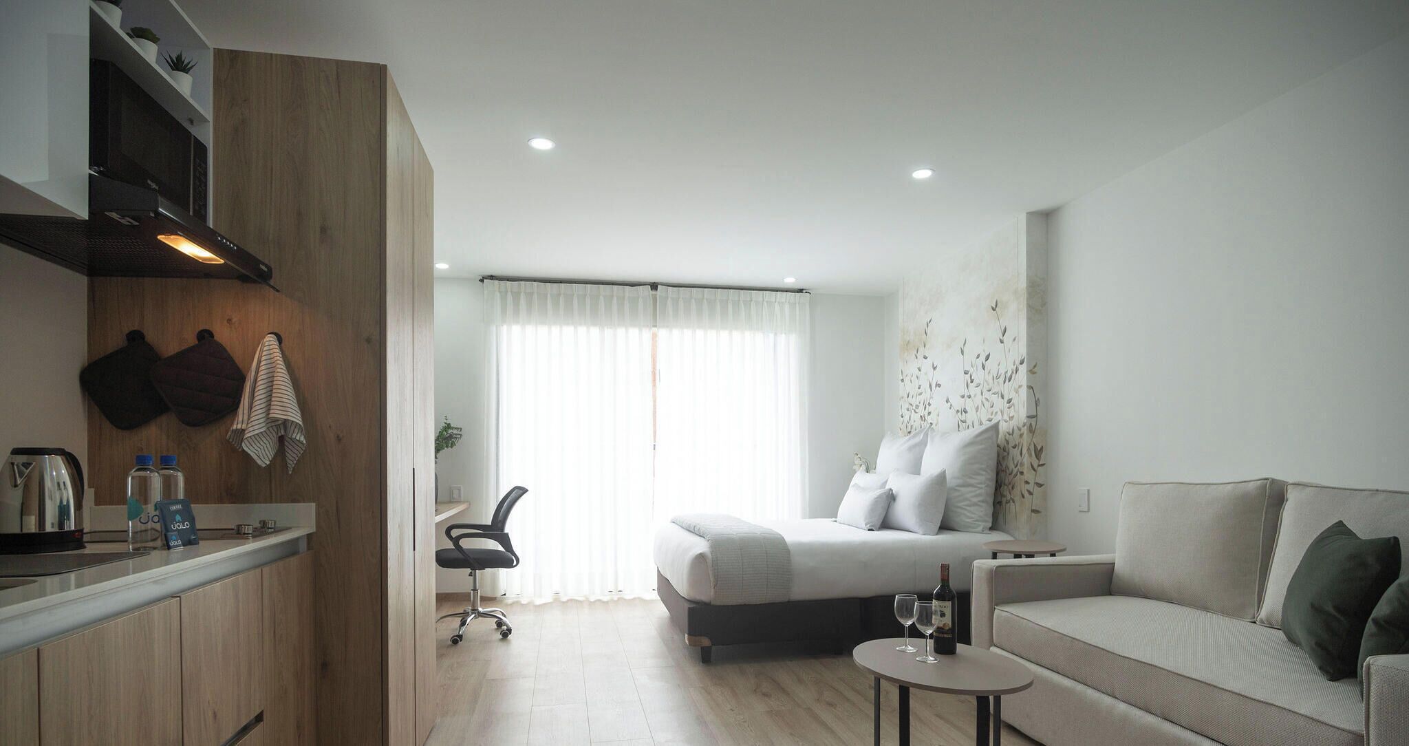 Una habitación de hotel moderna con una cama, un sofá, una mesita, un escritorio con hervidor y una silla.
