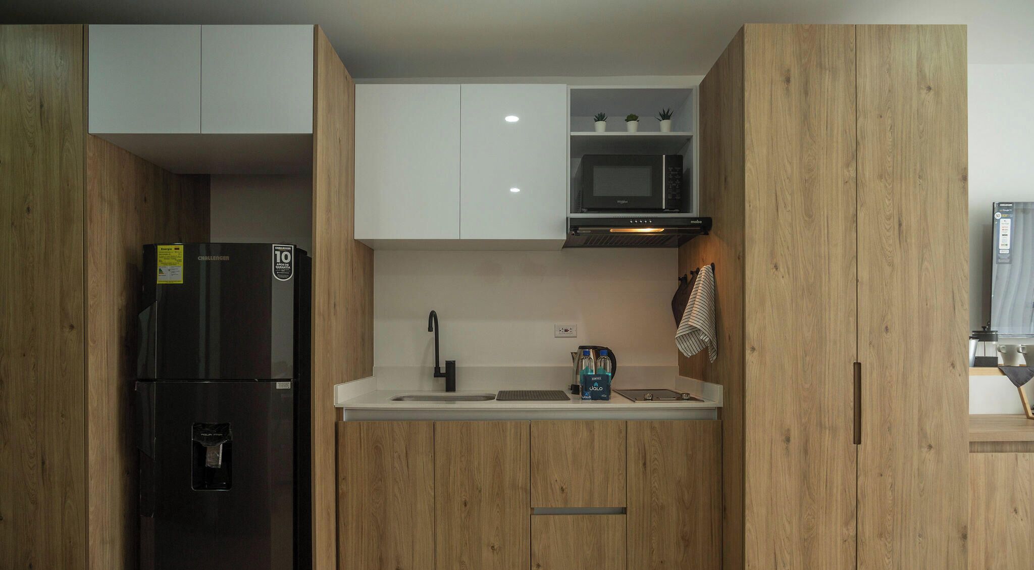 Una cuina moderna amb armaris de fusta, un refrigerador negre, un microones i una cafetera.