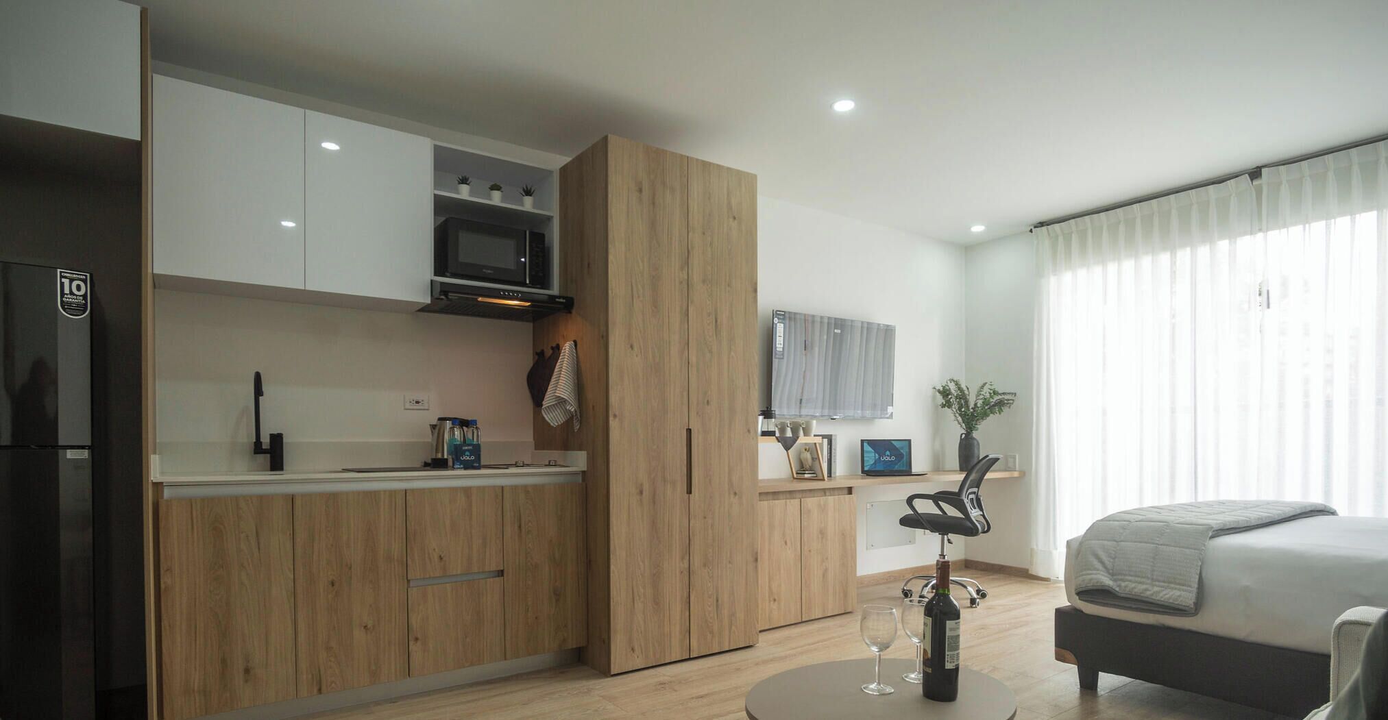 A compact kitchen with modern appliances, a dining area with a table and chairs, and a bedroom with a bed and curtains.