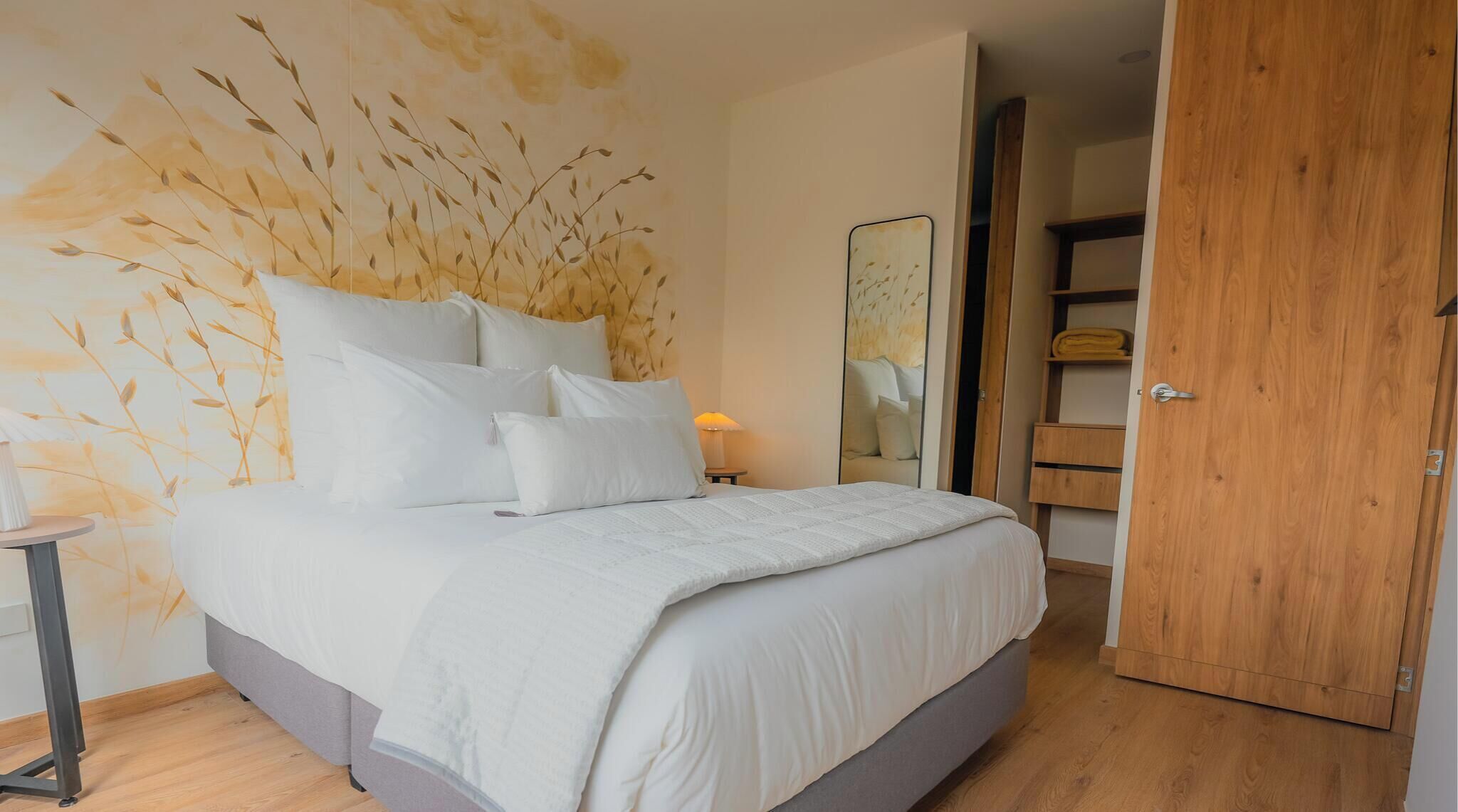 Quarto com cama, almofadas, mesa de cabeceira, luminária, guarda-roupa e espelho.