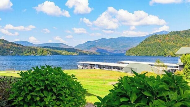 Une vue sur un lac, avec un bâtiment au premier plan, entouré d’une végétation luxuriante et des montagnes en arrière-plan.