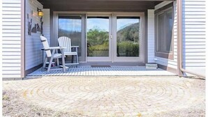 Un bâtiment doté d’un patio couvert comprenant deux chaises et une table, une porte-fenêtre coulissante et offrant une vue sur un paysage montagneux.