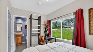 Une chambre à coucher comprenant un lit, un bureau, une chaise, une fenêtre avec des rideaux et une vue sur l’extérieur.